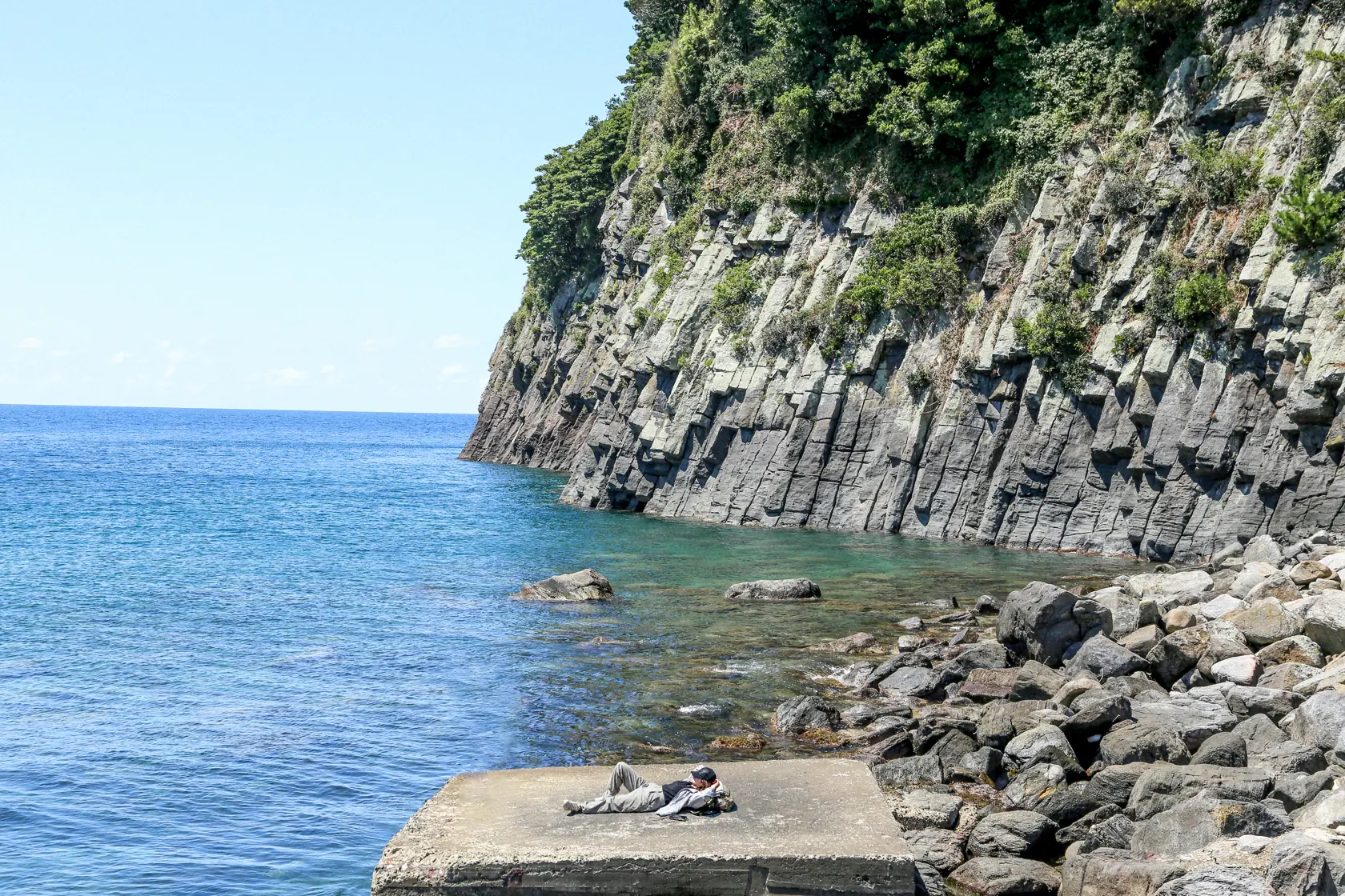 福井・三国の海岸の実写。柱状の岩壁と冬色の海、突堤にひとりの人物